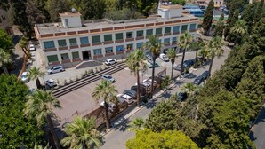 An aerial view of a multi-story building with a parking lot, surrounded by palm trees and other greenery. - Lady Hill (Taormina)