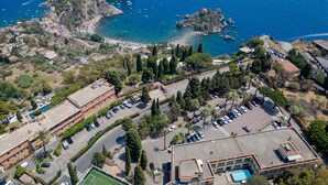 An aerial view of a coastal area with buildings, a parking lot, and a beach. - Lady Hill (Taormina)