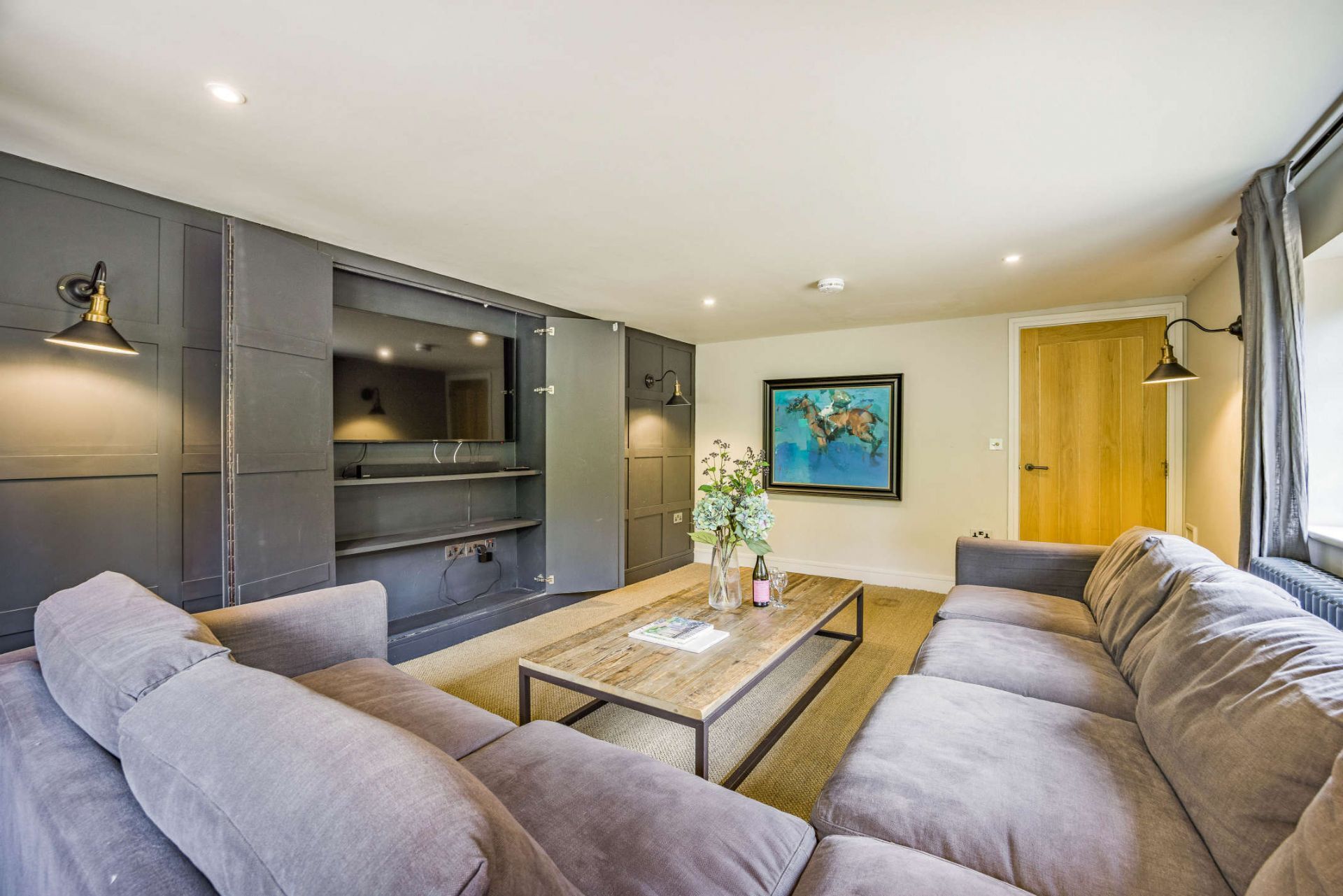 Un salon moderne avec un canapé gris, une table basse en bois et un grand téléviseur à écran plat fixé sur un mur gris foncé.