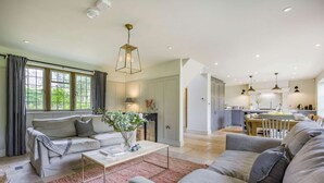 A modern living room with a sofa, coffee table, and a dining area with a table and chairs. - Large family friendly holiday home in the Cotswolds - Willows House (Lower Swell)