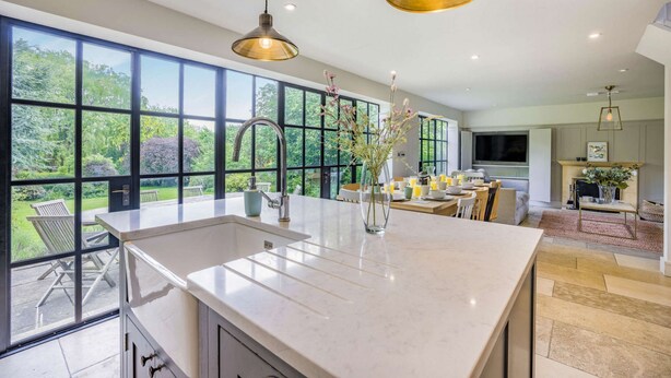 A modern kitchen with large windows, a central island, and a dining area with a TV. - Large family friendly holiday home in the Cotswolds - Willows House (Lower Swell)