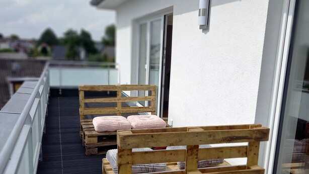 A rooftop terrace with wooden benches and a black floor, overlooking a residential area.
