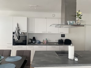 A modern kitchen with white cabinetry, a built-in oven, a coffee maker, and a glass shelf with decorative items.