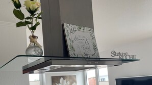 A modern living room with a glass-top dining table, a sofa, a TV, and a decorative vase with flowers.