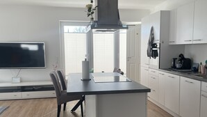A modern kitchen with a central island, white cabinetry, and a large window providing natural light.