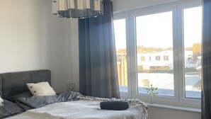 A modern bedroom with a large bed, grey bedding, and a view of the city through large windows.
