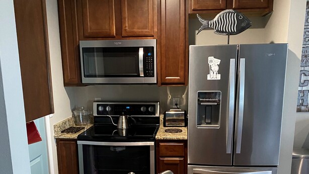 A kitchen with wooden cabinets, a stainless steel refrigerator, a microwave, an oven, and a granite countertop. - Welcome to Your New "HAPPY PLACE"   on your Island get away! (Navarre)