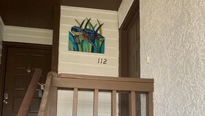 A wooden staircase with a white railing leading to a landing. A colorful painting of a snake and plants hangs above the landing, and the number 112 is displayed on the wall. - Welcome to Your New "HAPPY PLACE"   on your Island get away! (Navarre)