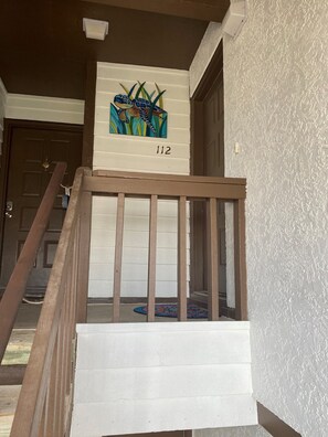 Uma escada de madeira com corrimão branco leva a um patamar. Um quadro colorido de uma cobra e plantas está pendurado acima do patamar, e o número 112 aparece na parede.