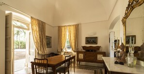 Ein Essbereich mit Holztisch, Stühlen und einem Schrank. Ein Fenster mit Vorhängen, ein Spiegel und eine Statue stehen auf dem Tisch.
