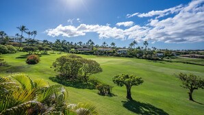 Un campo de golf con cielo despejado, palmeras y casas al fondo.