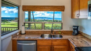Una cocina con encimeras de granito, armarios de madera, cafetera y vistas a un campo de golf.