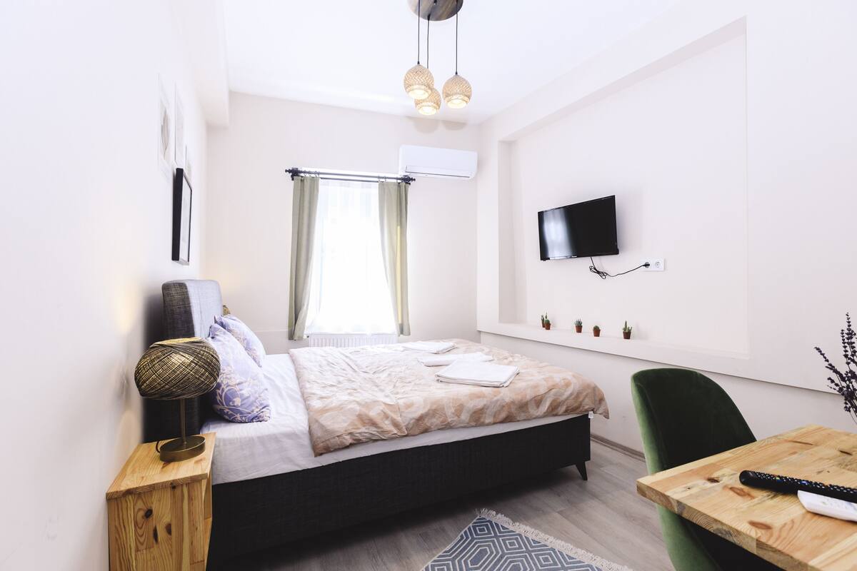 A modern bedroom with a bed, bedside table, lamp, TV, and a small table with a remote control.