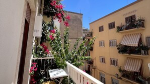 A balcony with a white railing, a small table, and chairs. There are potted plants and flowers on the railing.