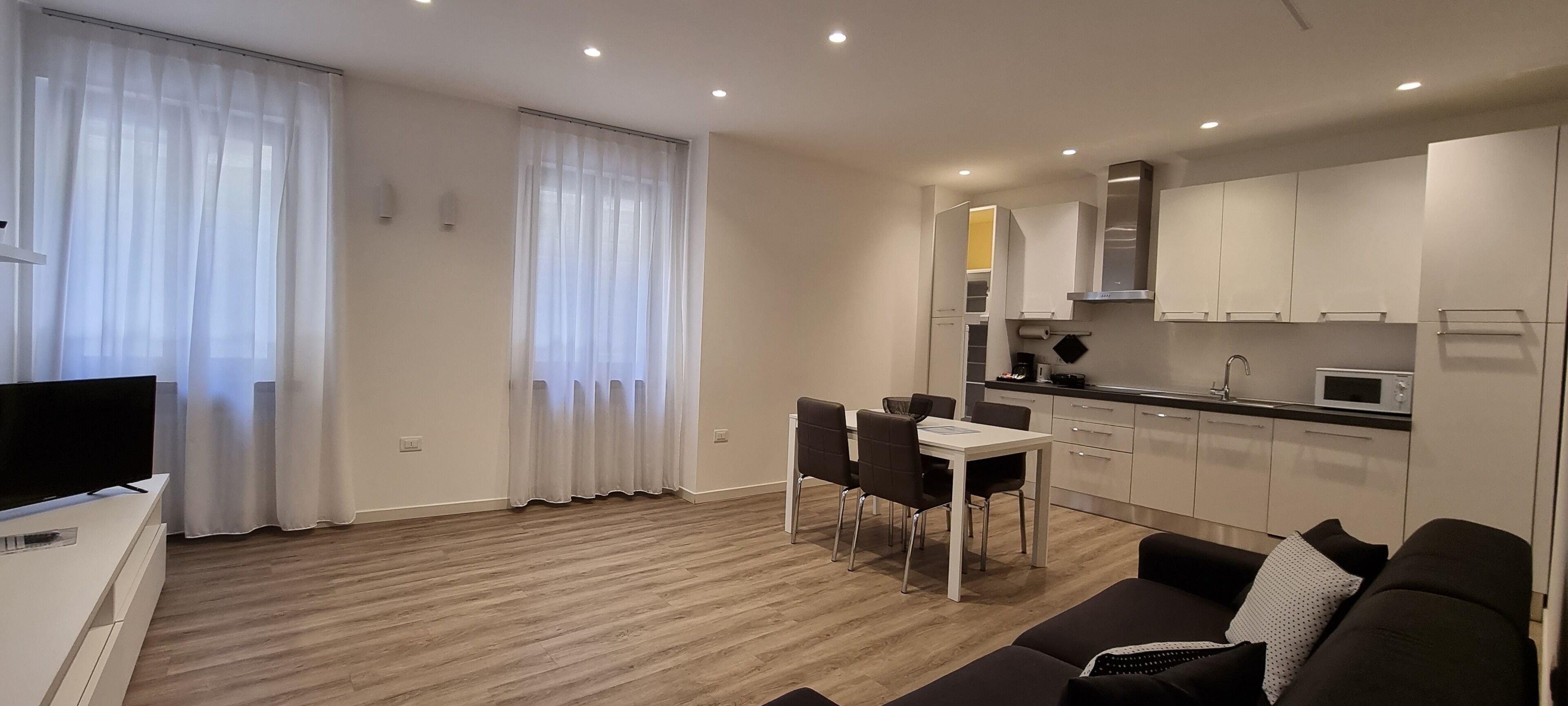 A modern living room with a flat-screen TV, a dining area with a table and chairs, and a kitchen with cabinets and appliances.