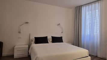Hotelkamer met een bed, twee bedlampjes, een nachtkastje, een stoel en een raam met gordijnen.