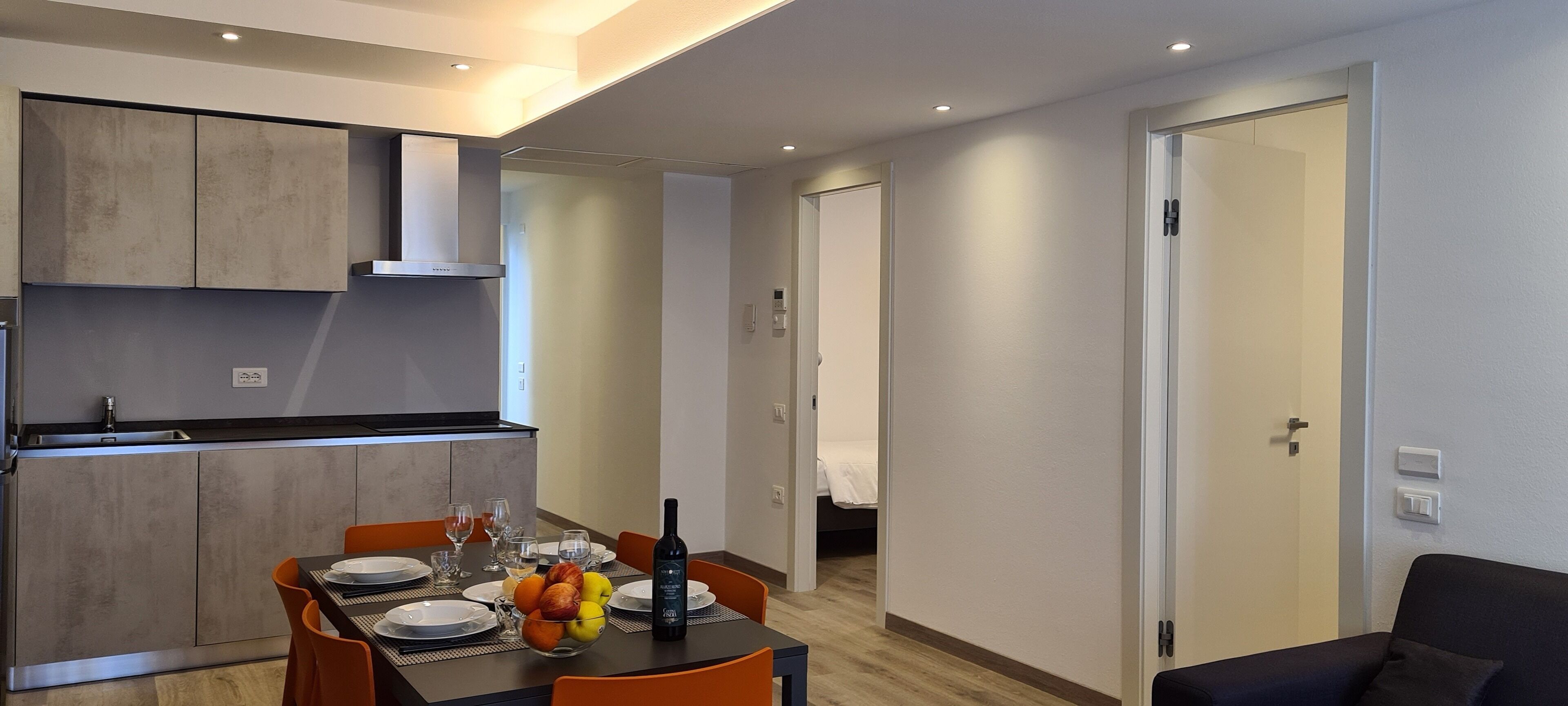 A modern kitchen with a dining area, a bed in the adjacent room, and a sofa in the living area.