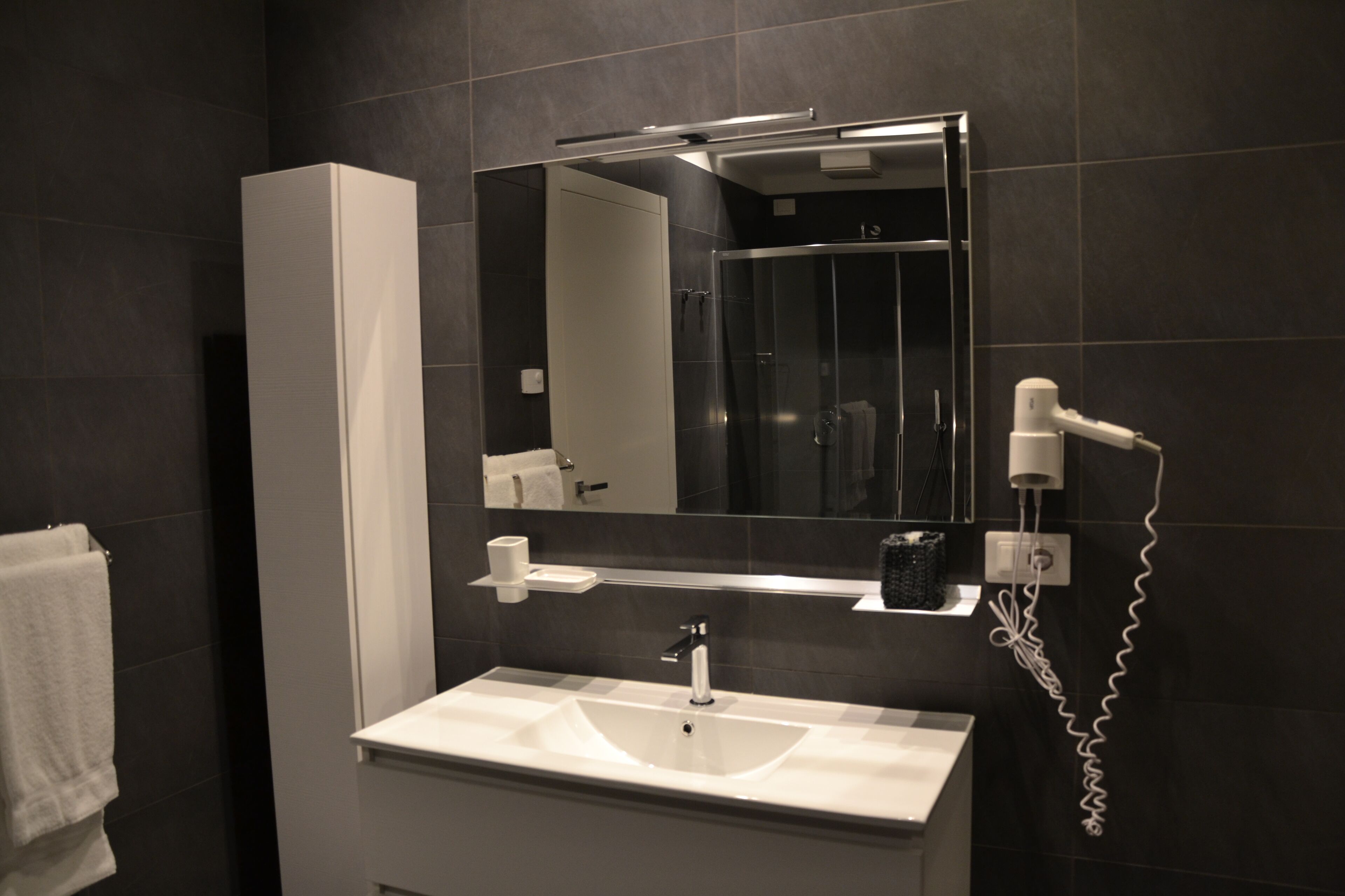 A modern bathroom with a white sink, a large mirror, a hairdryer, and a towel rack.