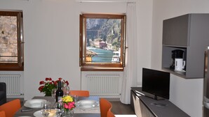 Ein Essbereich mit einem für vier Personen gedeckten Tisch, einem Fernseher und Blick auf eine Küstenstadt durch ein Fenster.