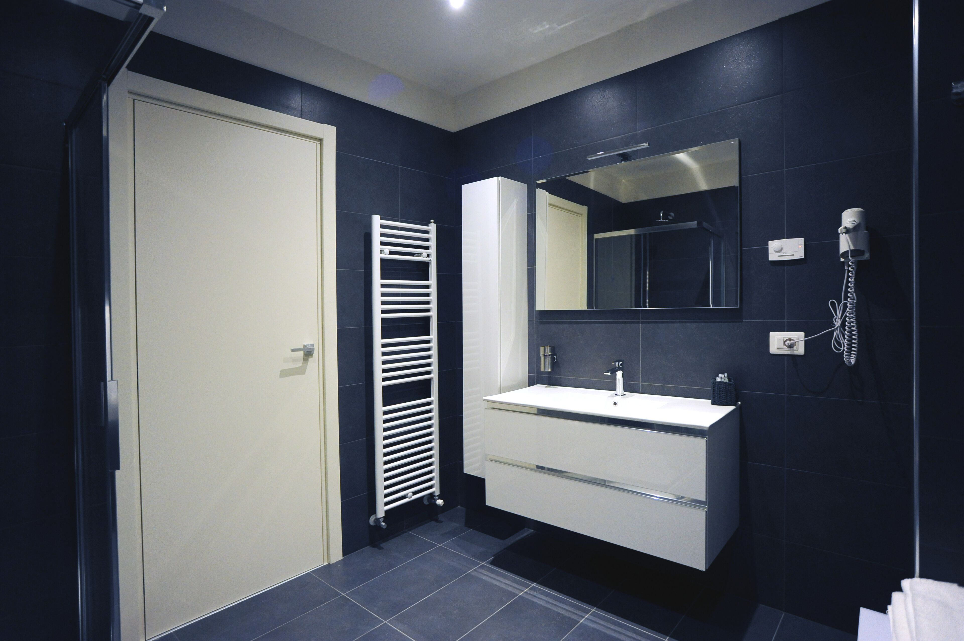A modern bathroom with a white vanity, a mirror, a towel rack, and a shower.