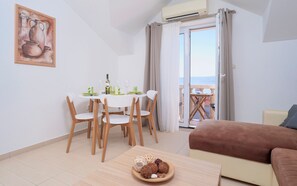 A dining area with a table set for two, a sofa, and a balcony with a view. - Hektorović (Bol)