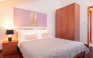 A neatly made bed with a white comforter and two pillows, a wooden nightstand with a lamp, a large wardrobe, and a framed artwork on the wall. - Hektorović (Bol)