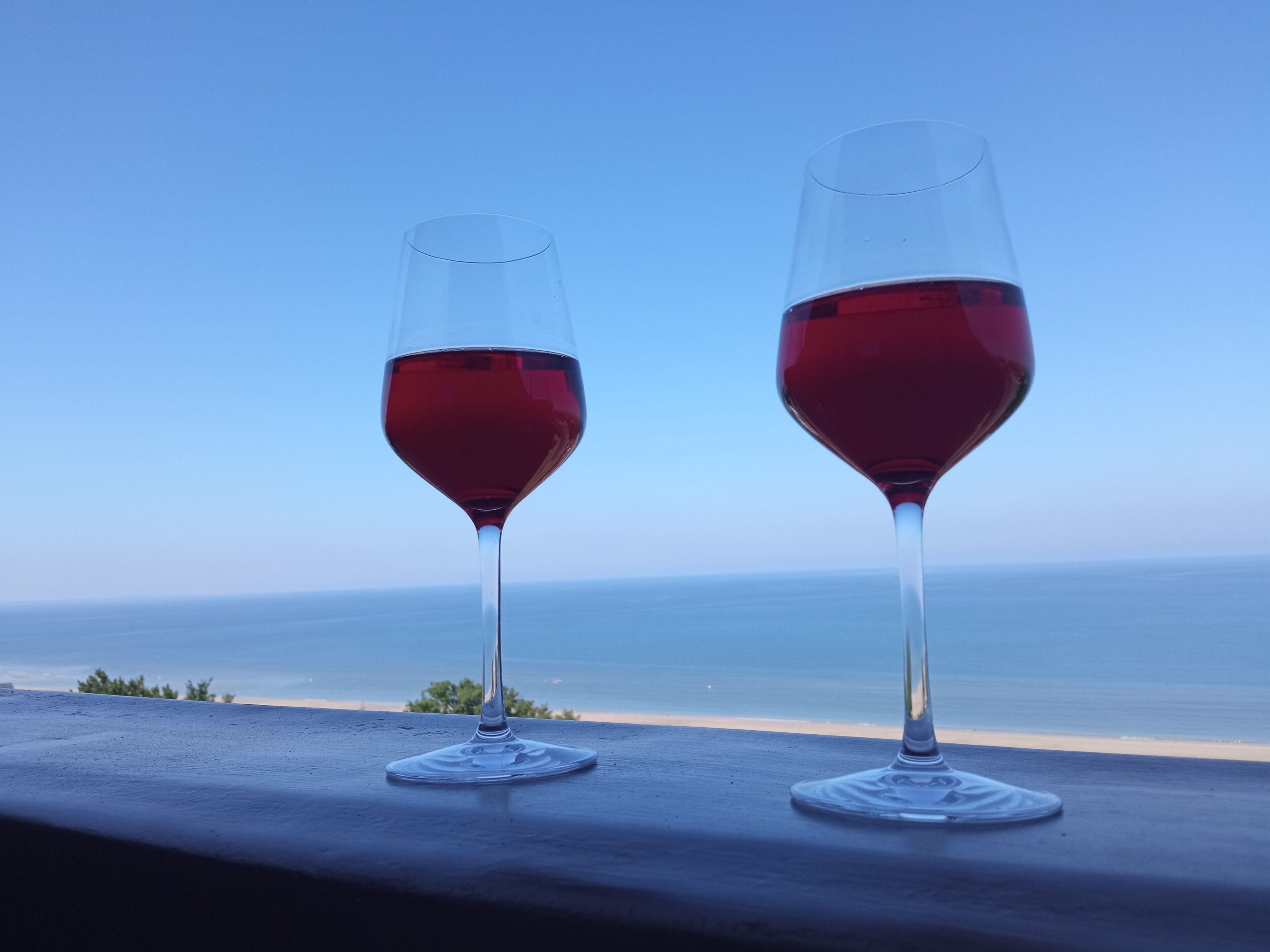 Two wine glasses on a balcony with a view of the ocean.