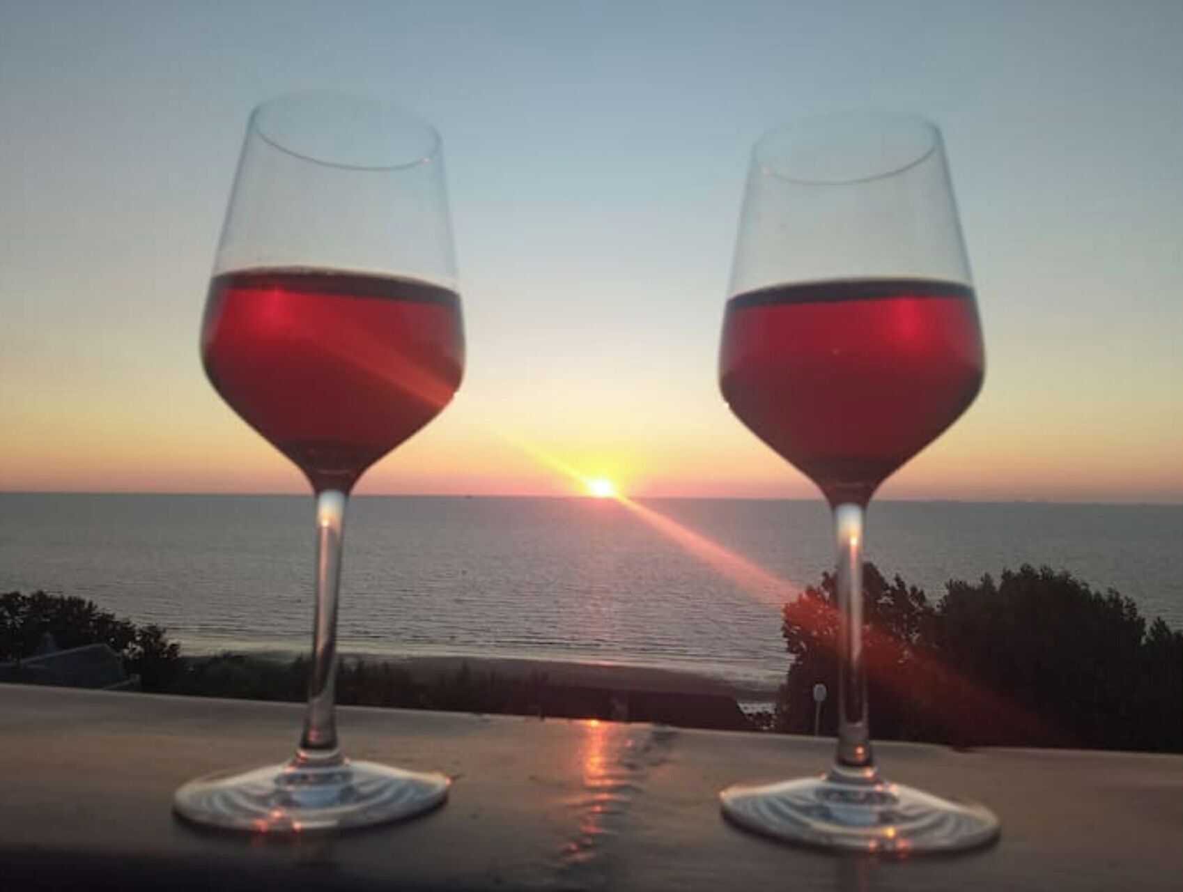 Dos copas de vino sobre una mesa, con vistas a la puesta de sol sobre el océano.