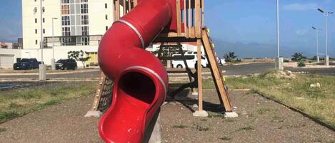 Un parque infantil con un tobogán rojo y una estructura de madera.