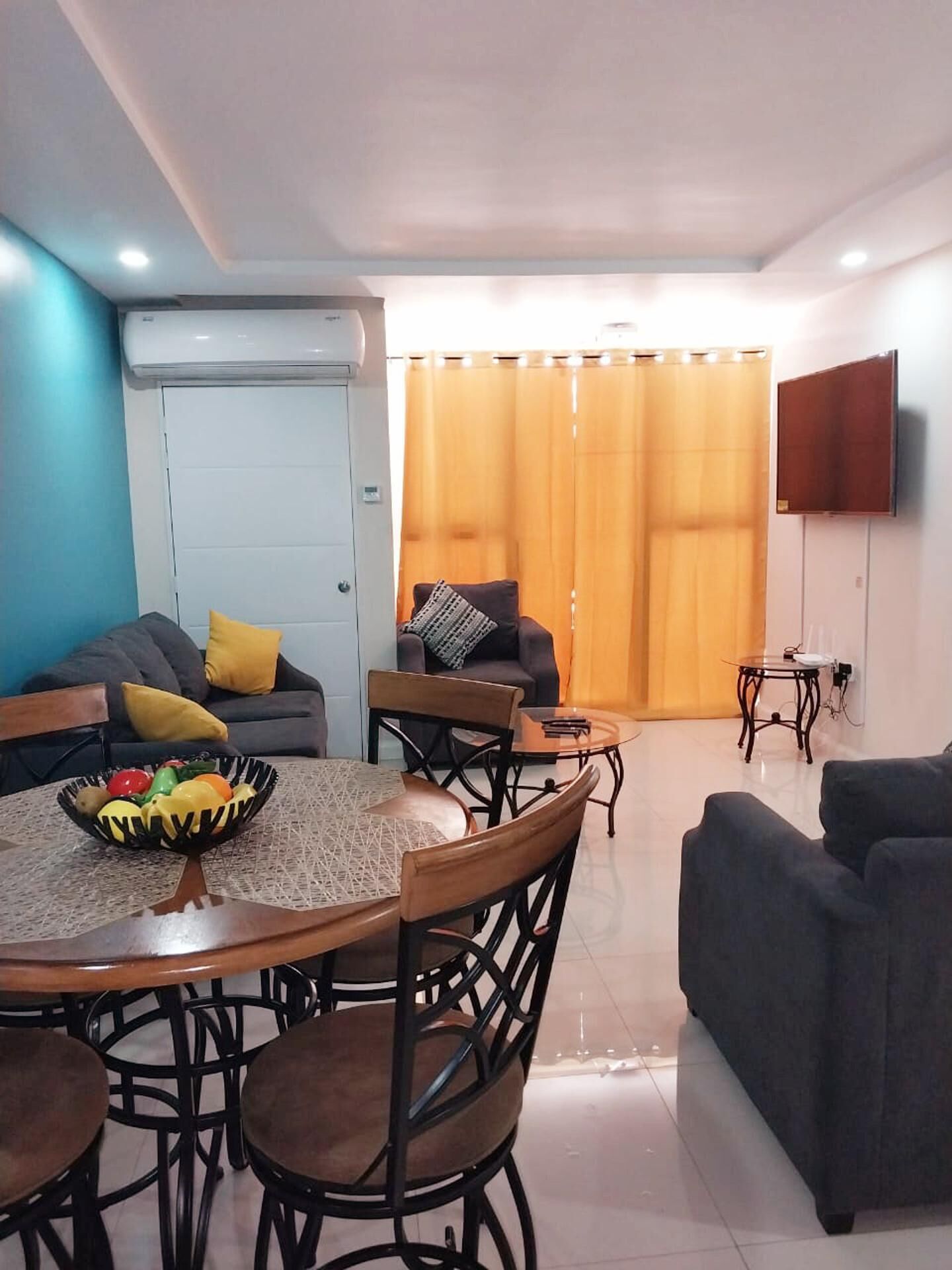 Un soggiorno moderno con zona pranzo, caratterizzato da un tavolo rotondo, sedie, divani e una TV a parete.
