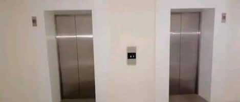 Dois elevadores em um corredor com piso claro.