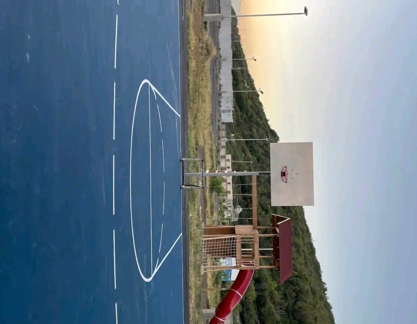 A parking lot with a basketball court, a red slide, and a guardrail.