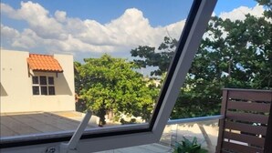 A balcony with two chairs, two potted plants, and a view of a building with a red roof. - Ornella Villa - 2-br Apartment - Pool - Parking (Portmore)