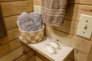 A wooden cabin-style bathroom with a wooden tub, a towel rack with a towel, and a wooden shelf with toiletries.