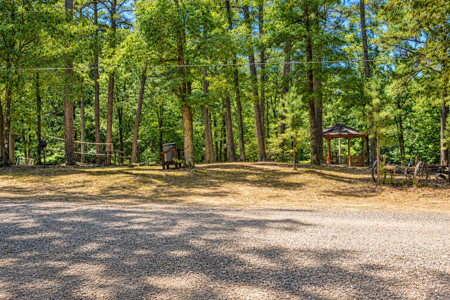 A campground with a gazebo, picnic tables, and a gravel path.
