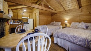 Uma cabana aconchegante com paredes de madeira, área de jantar com mesa e cadeiras, e duas camas com roupa de cama estampada.