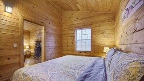 Quarto de cabana de madeira com uma cama, uma janela e uma porta que dá para o banheiro.