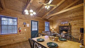 Interior de cabana de madeira com mesa de jantar posta para quatro pessoas, lareira e um espaço de estar aconchegante.