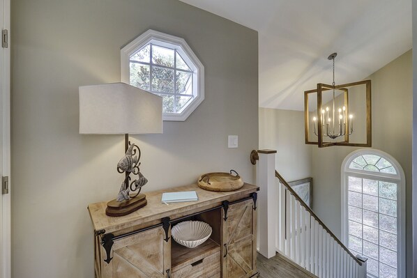 Un couloir avec une console en bois, une sculpture de poisson, une lampe blanche, un bol en bois et un miroir.