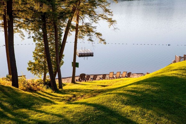A lakeside area with a dock, chairs, and a grassy slope.
