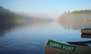Un lac paisible, avec un bateau portant l’inscription « Sunny Point » amarré sur la droite.