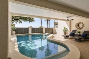 An indoor swimming pool with a curved design, surrounded by lounge chairs and potted plants.
