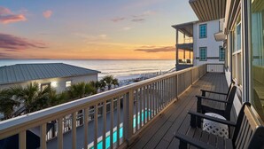 A balcony with a view of the ocean at sunset, a pool, and a building with multiple windows. - Gulf Views with Pool, Firepit and LSV (Santa Rosa Beach)