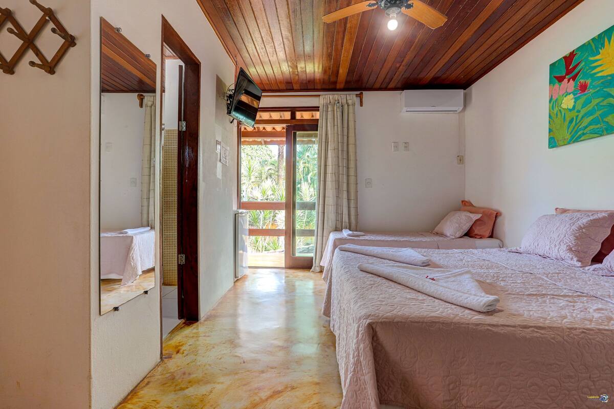 Quarto com duas camas, teto de madeira, ventilador de teto e vista para o verde lá fora.