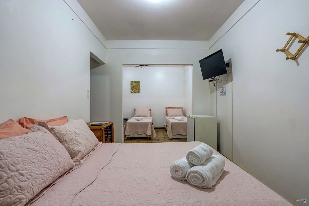 Quarto de hotel com uma cama grande, duas camas menores, uma TV e um espelho.