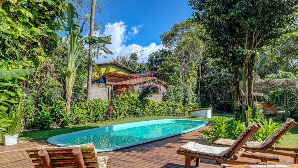 Terraza de madera con sillones de descanso, piscina y abundante vegetación.
