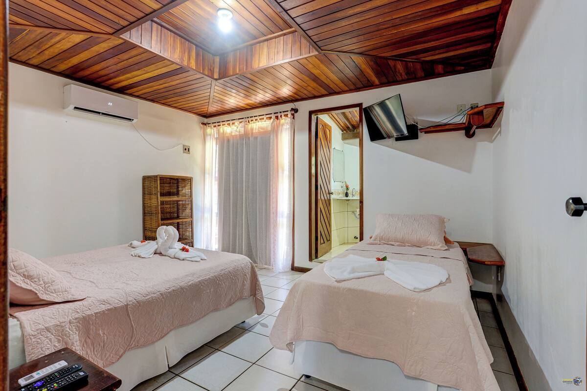 Quarto de hotel com duas camas, teto de madeira, televisão na parede e banheiro visível por uma porta.