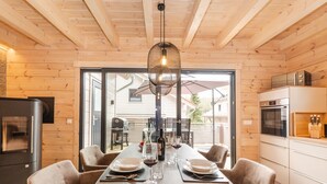A modern kitchen with wooden walls, a dining table set for four, and a view of the outside. - Bergwaldchalets Wellness (Wernigerode)