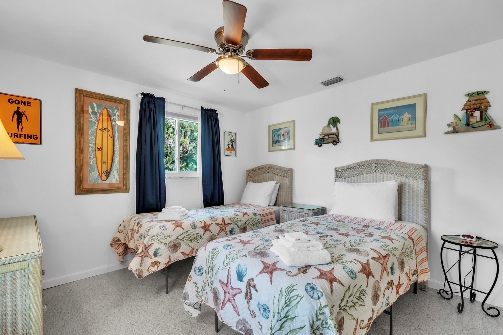 A bedroom with two beds, a ceiling fan, and various wall decorations including a surfing sign and framed pictures.
