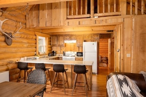 A log cabin interior with a kitchen, dining area, and a cozy living space.